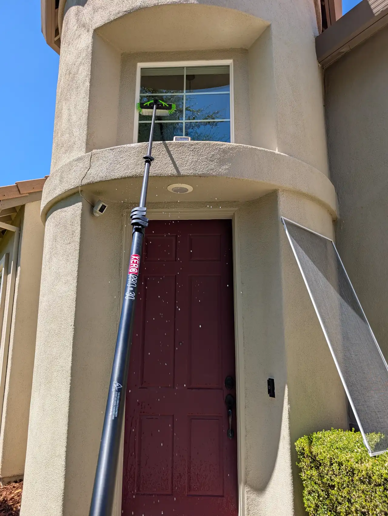 A water-fed pole with a brush reaching a second-story window above a dark red front door.