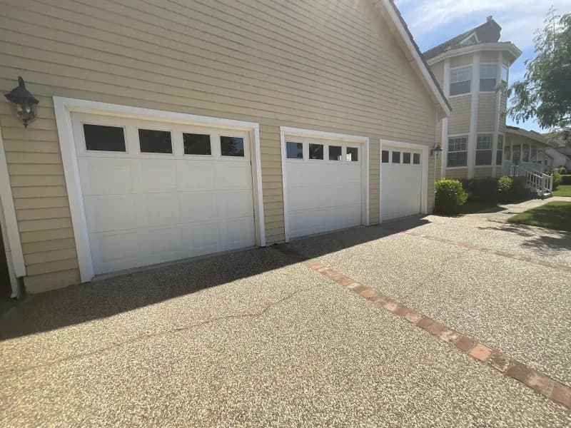 A three-car garage door and driveway at the side of the reviewer's house, photographed in hard midday sun.