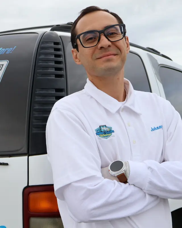 Johnny standing beside his white work truck under an overcast sky. The truck's side reads Johnny Cleans Windows in blue and yellow lettering, with the services listed underneath and the website address along the bottom of the door.